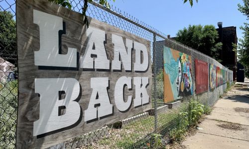 Mural that reads 'Land Back' with Indigenous artwork along fence