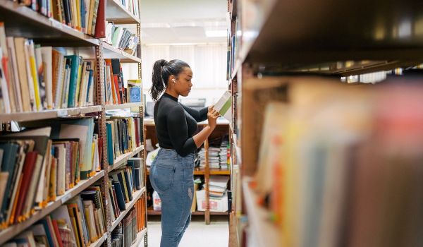 Patron stands in the aisle of a library and looks at books