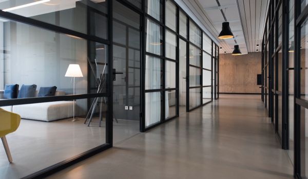 Hall way of an office building with glass windows and doors on both sides; a couch and chair can be seen on the left