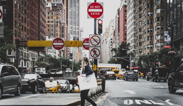 Person walks in a crosswalk in New York City. Cars and traffic signs can be seen in background.